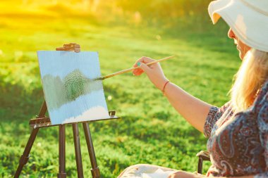 yaşlı bir kadın doğada bir resim boyar