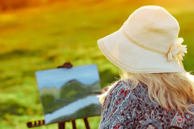 yaşlı bir kadın doğada bir resim boyar