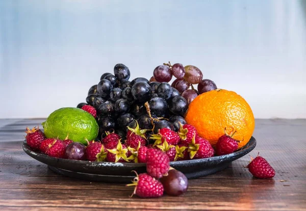 Salada de frutas deliciosas em prato na mesa, limão, framboesa, uvas — Fotografia de Stock