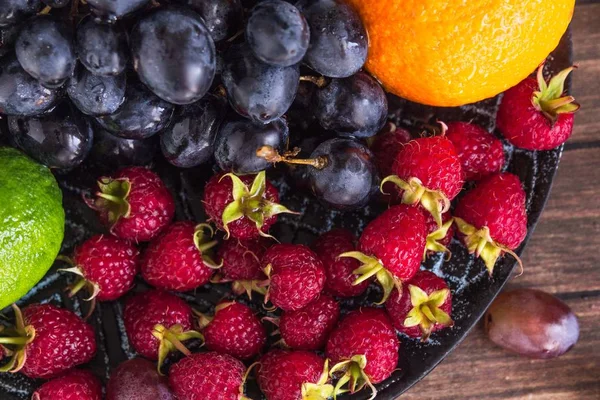 Primer plano de ensalada de frutas con frambuesas, uva, lima en un plato de arcilla sobre una mesa de madera rústica, vista desde arriba, macro — Foto de Stock