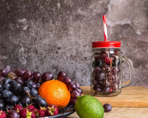 Turmix üveg alakú gyümölcsök. Szőlő, málna, lime, sötét háttér — Stock Fotó