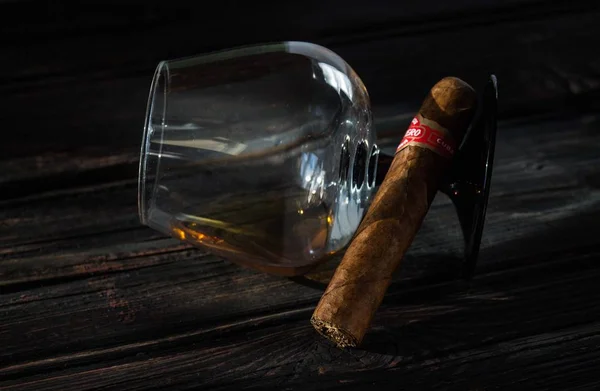 Szklanka brandy i kubańskie cygaro na starym drewnianym stole. — Zdjęcie stockowe