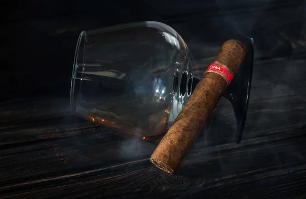 Glas brandy og cubansk cigar på et gammelt træbord. - Stock-foto