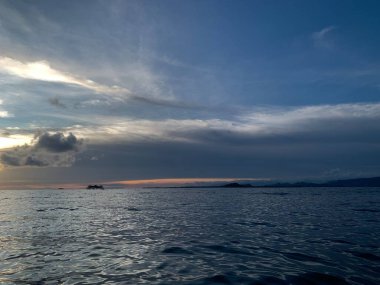 sunset over the ocean with a backdrop of clouds and mountains.
