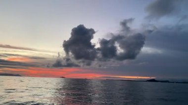 View of sunset over the ocean with black clouds.