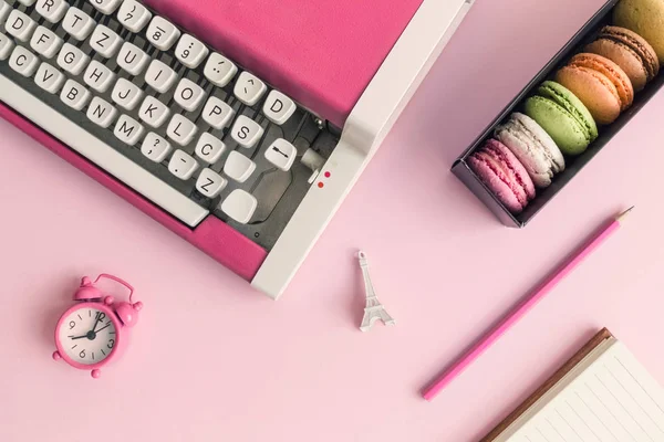 Flat lay of typewriter, macaroons, alarm clock, Eiffel Tower miniature and notebook with pencil pink minimal creative concept.