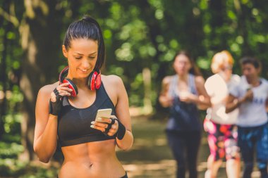 Genç kadın koşu ve akıllı telefon doğada kullanarak sonra rahatlatıcı. Koşucular içinde belgili tanımlık geçmiş.