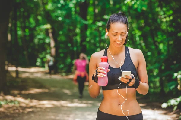 Female runner holding smart phone and listening her favorite song in nature.