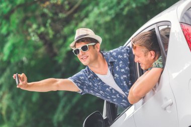 Doğada araba pencereden selfie alarak neşeli hipster arkadaşlar. Yol ve teknoloji kavramı üzerinde seyahat.