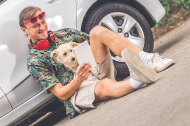 Araba yanında oturan ve dijital tablet cihaz zekâ köpeğini arıyor hipster.