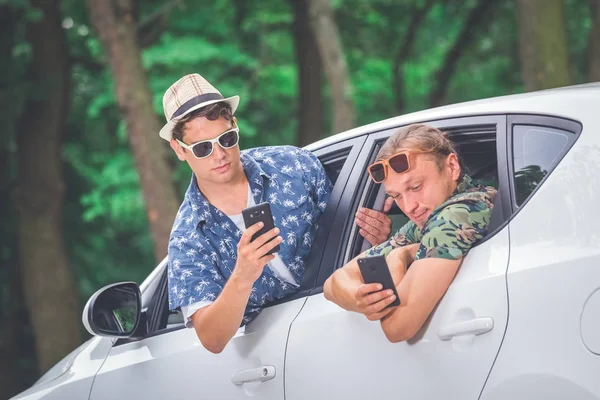 Two hipsters using their smart phones out of car windows. Travel on the road trip and technology concepts.