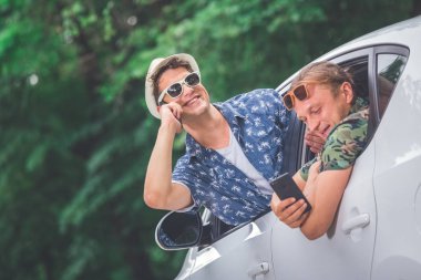 İki hipsters araba camdan akıllı telefonlarını kullanarak. Yol çelme takmak ve teknoloji kavramları üzerinde seyahat.