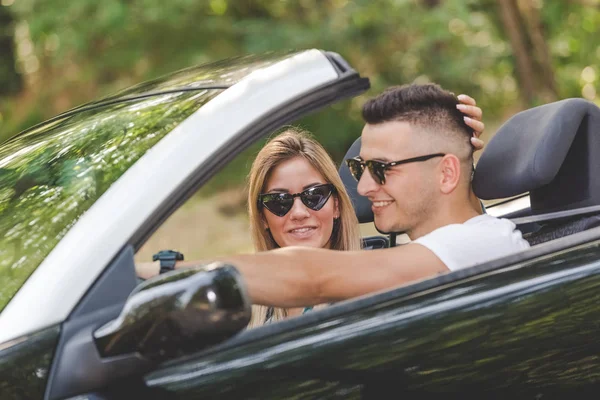 Young couple enjoying road trip inside of their convertible car.