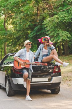 Genç moda çift doğada kendi Cabrio araba arka tarafındaki akustik gitar çalmak.