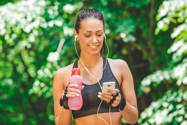 Female runner holding smart phone and listening her favorite song in nature.