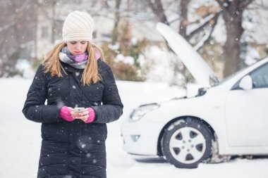 Yol yardımı hizmeti aramak için akıllı telefon kullanan genç kadın. Kış ve araç konsepti.