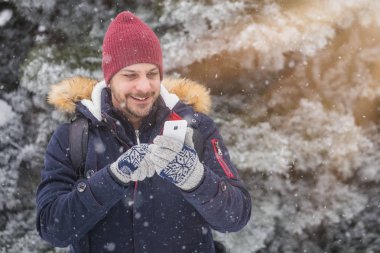 Karlı gününde smartphone kullanan genç adam portresi.