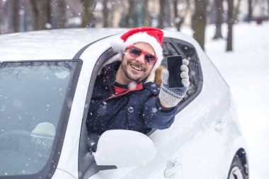Santa şapka ve güneş gözlüğü boş ekran smartphone gösterilen sürücü. Kış tatil ve seyahat kavramı.