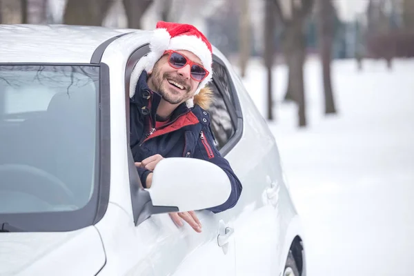 Araç sürücüsü ile Noel Baba şapkası araba penceresinden portresi. Yol kış tatil ve tatil konsepti üzerinde.