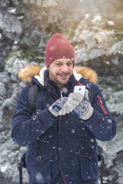 Karlı gününde smartphone kullanan genç adam portresi.