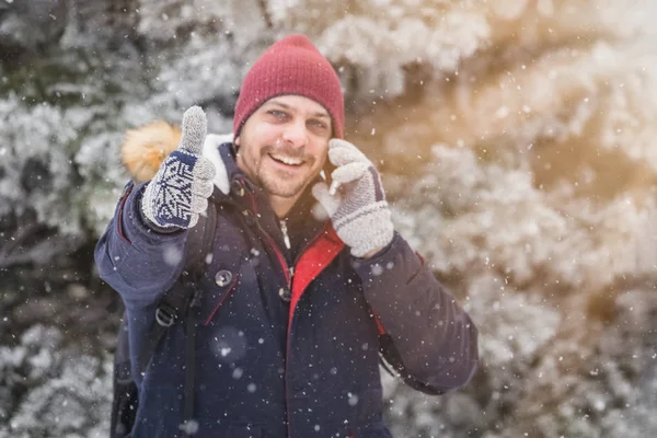 Smartphone kullanarak ve karlı gününde başparmak gösterilmesini genç adam portresi.