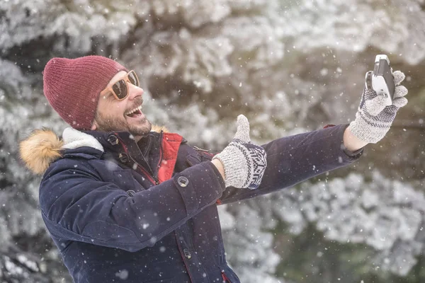 Mutlu adam selfie başparmak ile kış arka plan üzerinde çekici yukarıya.