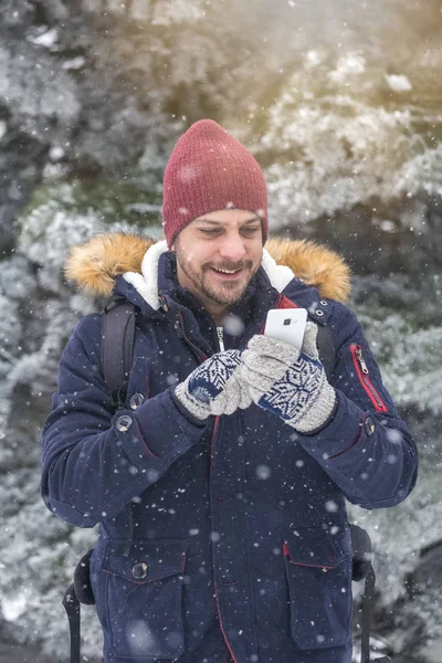 Karlı gününde smartphone kullanan genç adam portresi.