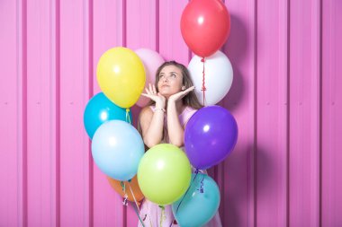 Pastel pembe bir arka plan üzerinde renkli balonlu güzel genç kadın.