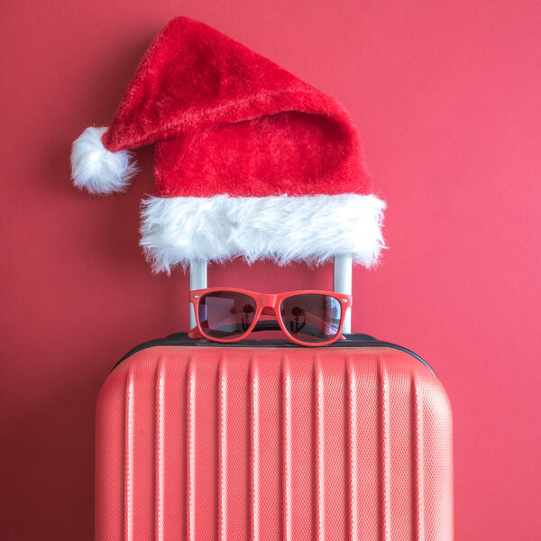 Suitcase with Santa hat and sunglasses on red background minimal creative concept.