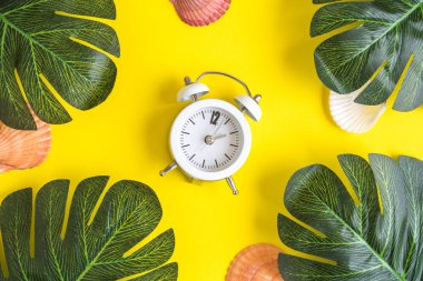 Tropikal palmiye yaprakları ve sarı zemin üzerine kabukları ile küçük korku masa saati. Yaz aylarında en az yaratıcı kavramı.