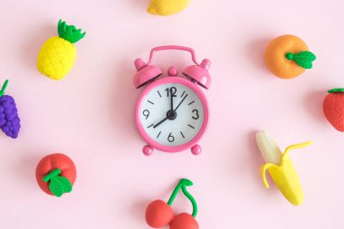 Pastel pembe arka plan en az yaratıcı kavramı çalar saat ve kauçuk meyve model düz yatıyordu.