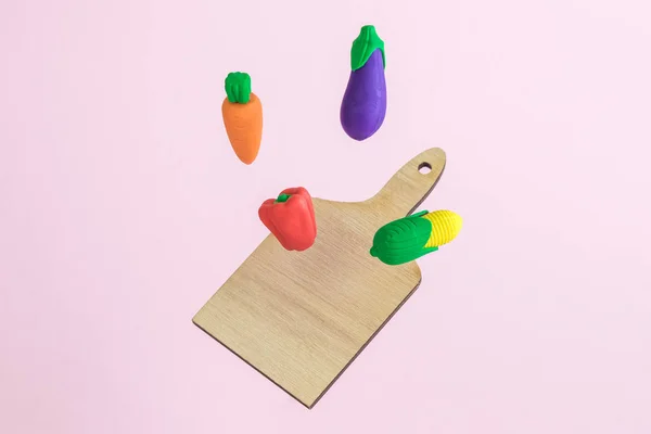 Flying vegetables with wooden cutting board abstract on pastel pink background minimal food preparation cooking creative concept.