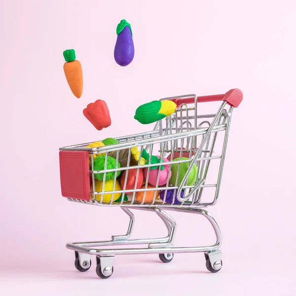 Carrot, eggplant,pepper and corn falling into shopping cart with fruits and vegetables abstract isolated on rose.