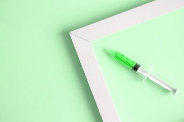 Şırınga ve resim çerçevesinin izole yeşil arka plan en az yaratıcı kavramı üzerinde düz lay.