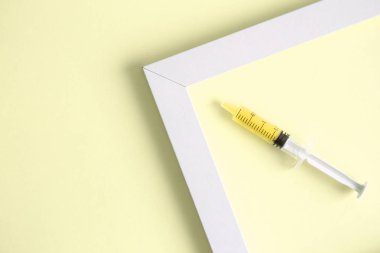 Şırınga ve resim çerçevesinin izole sarı arka plan en az yaratıcı kavramı üzerinde düz lay.