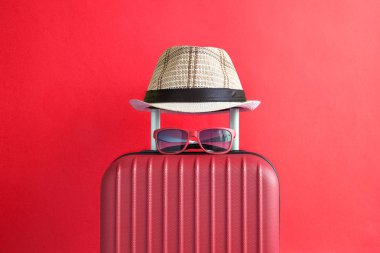 Şapka ve güneş gözlüğü üzerinde kırmızı bir arka plan en az yaratıcı bavul seyahat kavramı