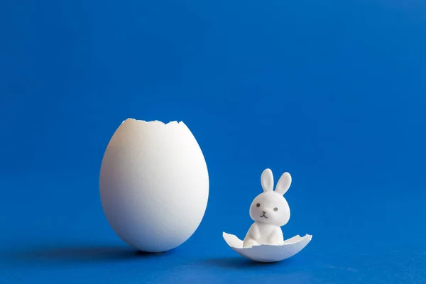 Cáscara de huevo blanca y juguete de conejo abstracto sobre fondo azul . — Foto de Stock