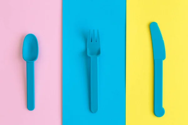 Colocación plana de cuchara de plástico, tenedor y cuchillo sobre fondo colorido concepto creativo mínimo . — Foto de Stock
