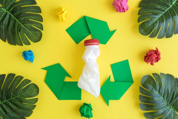 Sinal de reciclagem com garrafa de plástico e folhas de palma tropicais com papel amassado em amarelo . — Fotografia de Stock