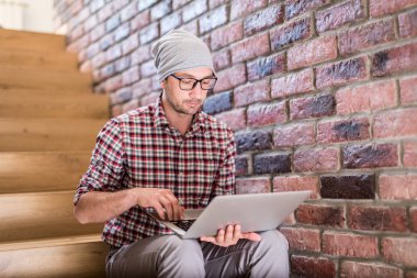 Modern hipster portresi merdivenlerde oturan ve onun dizüstü üzerinde çalışan.