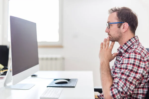 Molesto empresario moderno sentado en el escritorio y mirando en pantalla en blanco monitor de ordenador de escritorio . — Foto de Stock