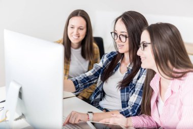 Bir grup genç kız öğrenci masada oturarak ve bilgisayar başında çalışıyor.