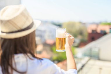 Arka planda şehir binalarına karşı bira cam tutan sunhat moda kadın.