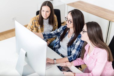 Bir grup genç kız öğrenci masada oturarak ve bilgisayar başında çalışıyor.