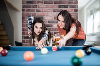 Bilardo oyunu oynayan ve bira içen iki kız öğrenci.