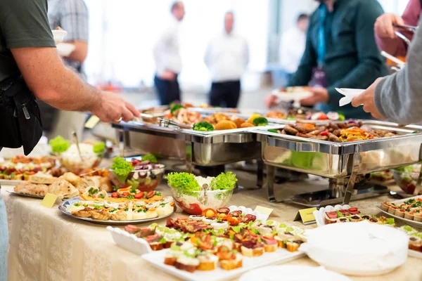 Restoran büfesinde kanepeler ile kendilerine hizmet veren insanlar yakın.