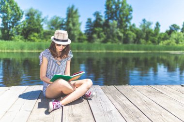 Ahşap rıhtımda dinlenen şık kadın ve kitap okuma.