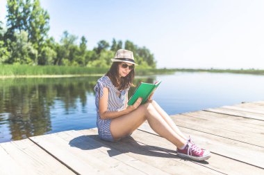 Ahşap rıhtımda kitap tutan kızın portresi.