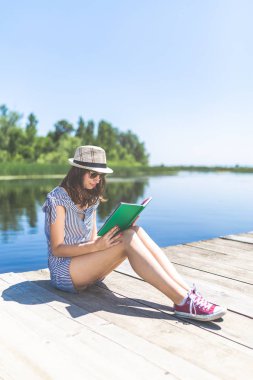 İskelede dinlenen ve kitap okuyan bir kadın..