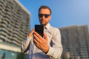 Yakışıklı yönetici modern binalara karşı akıllı telefon bakıyor.
